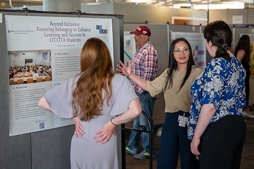 a student explaining her poster to onlookers a student explaining her poster to onlookers